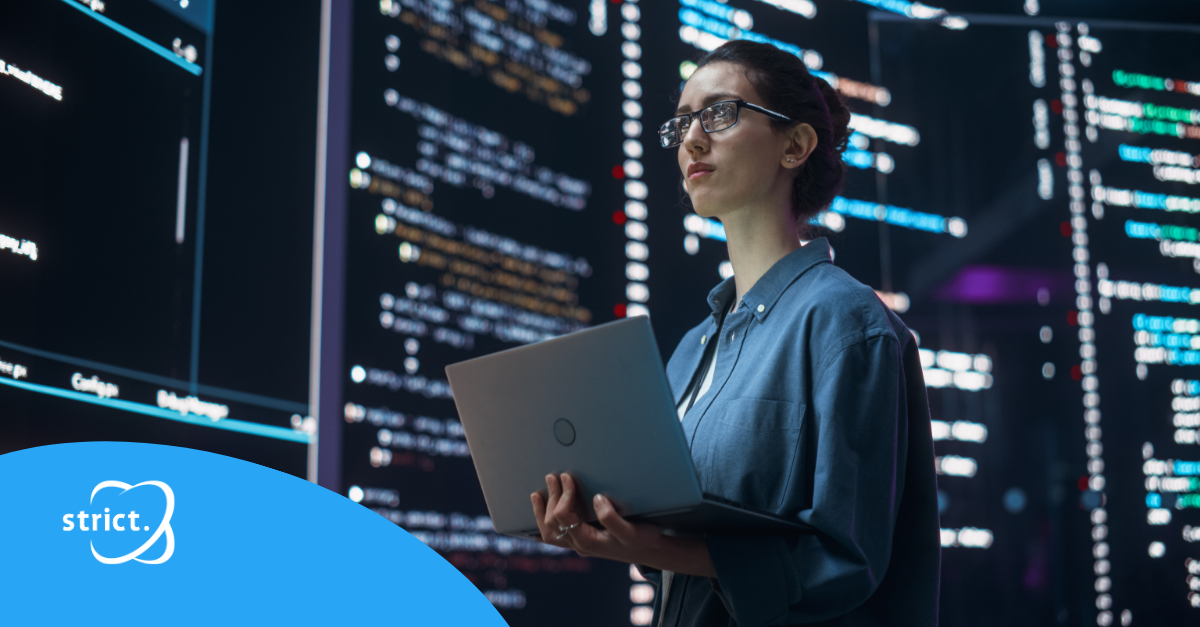 Persoon met een laptop staat voor grote schermen in een moderne, technologische werkomgeving.